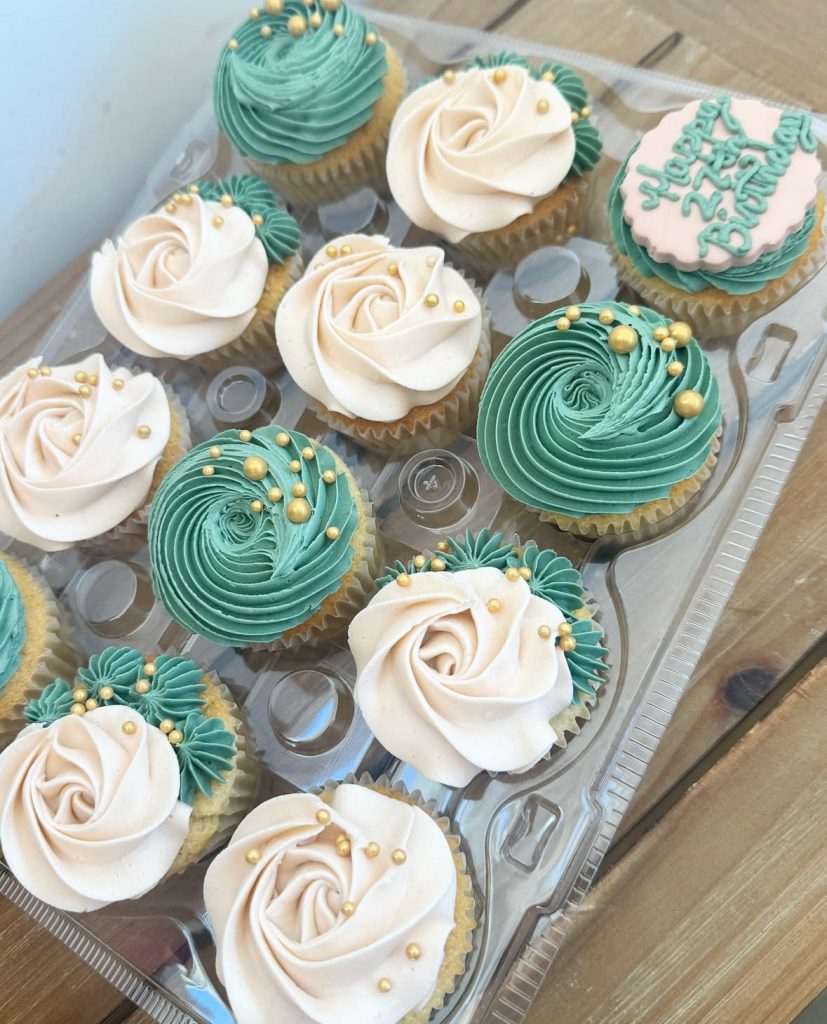 cupcakes with white and green frosting with gold sprinkles in a plastic container