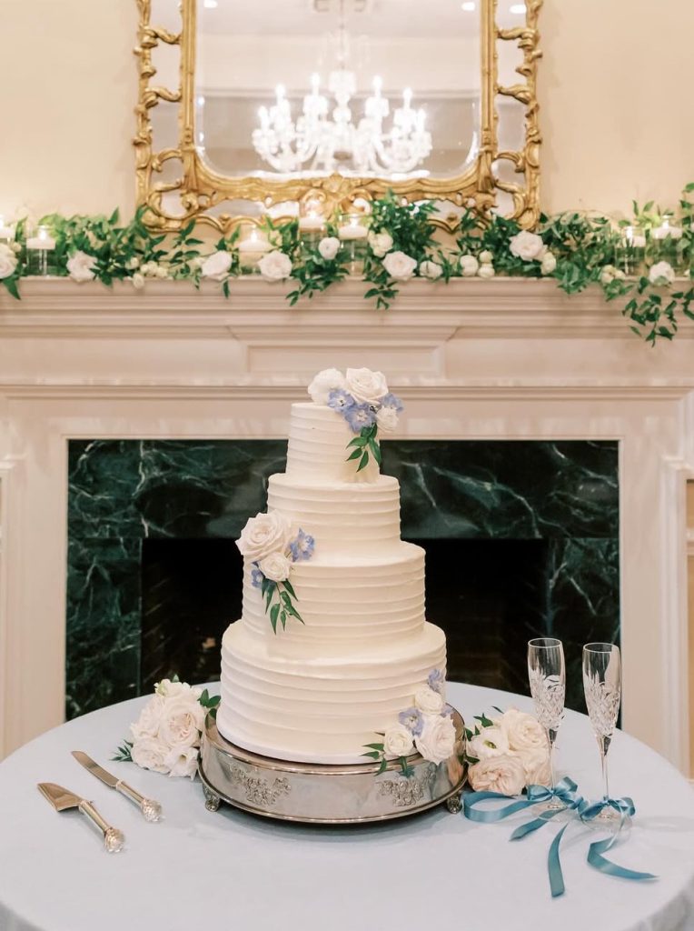 4 tier wedding cake with blue flowers on a table with wedding decor