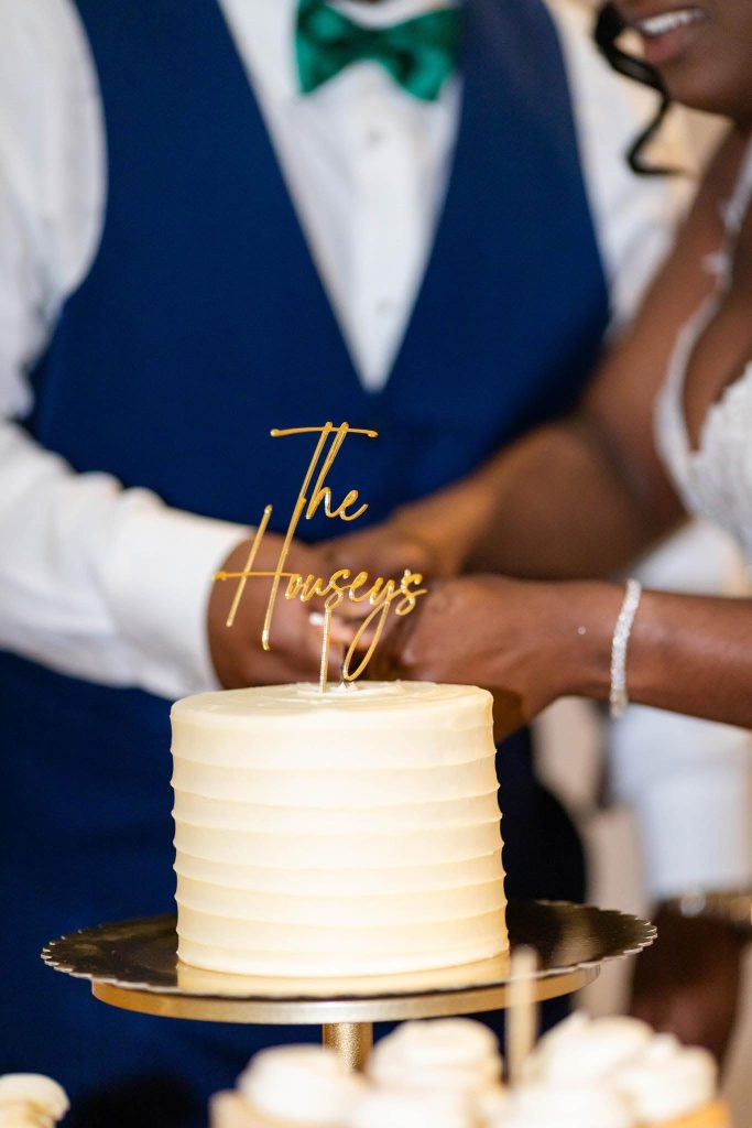 A wedding cake with a decoration on top being cut by a couple at their wedding